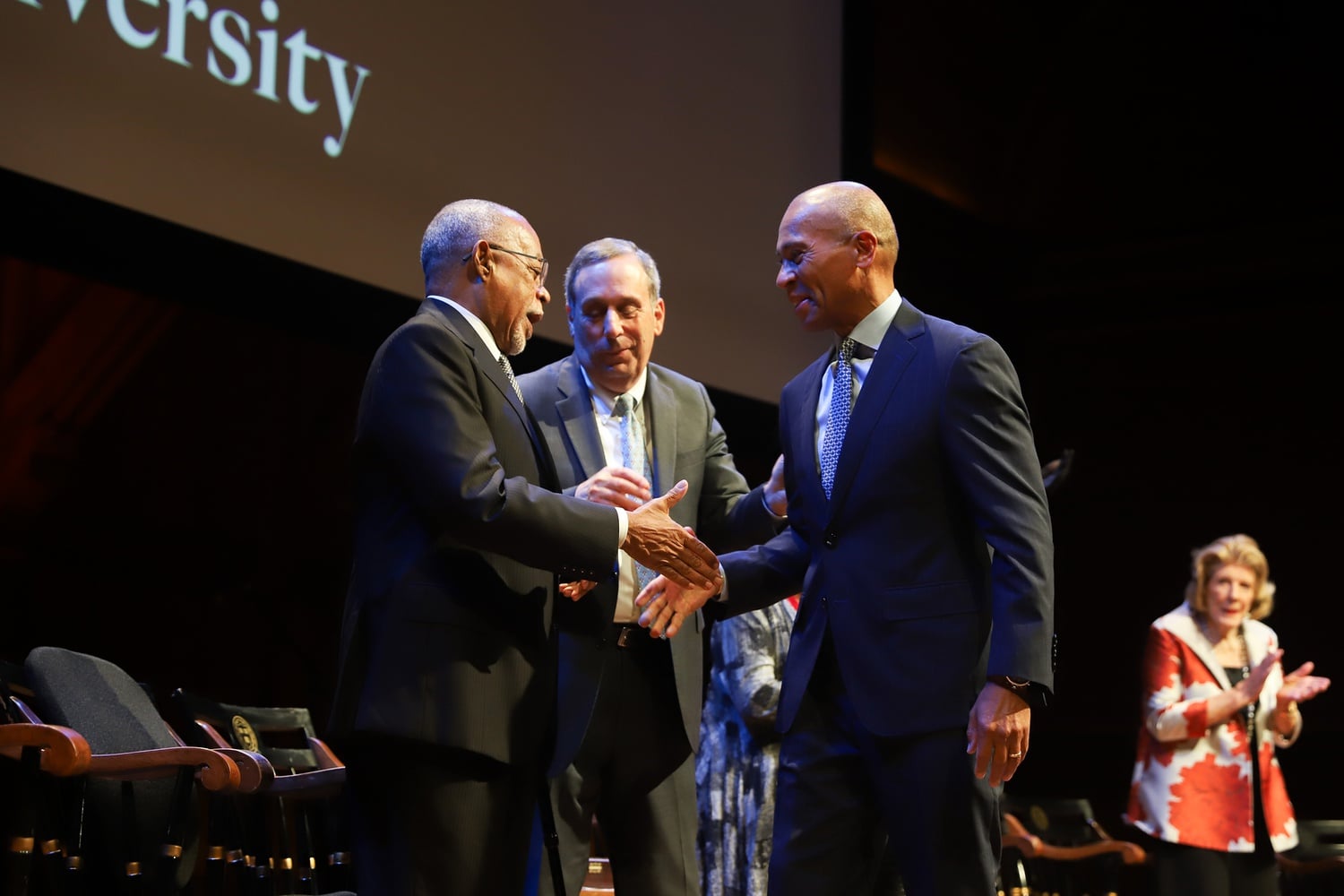 University professor Henry Louis Gates Jr., left, shakes hands with former Massachusetts Governor Deval L. Patrick ’78, right, as Harvard Preside Lawrence S. Bacow looks on.