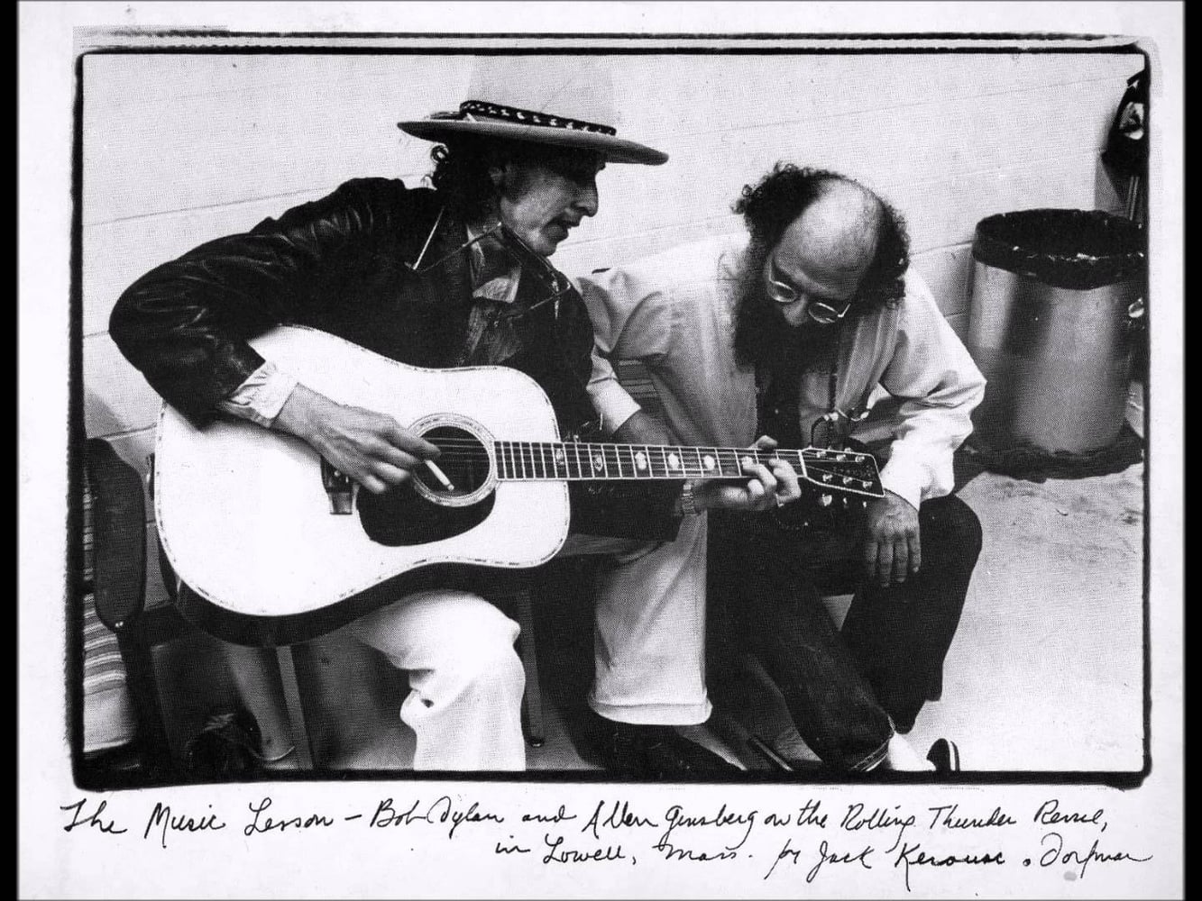 Allen Ginsberg looks down at Bob Dylan’s left hand as Dylan shapes a D chord on his fretboard, casually holding a cigarette in his other hand. This photo hangs in Harvard’s Office of the President.