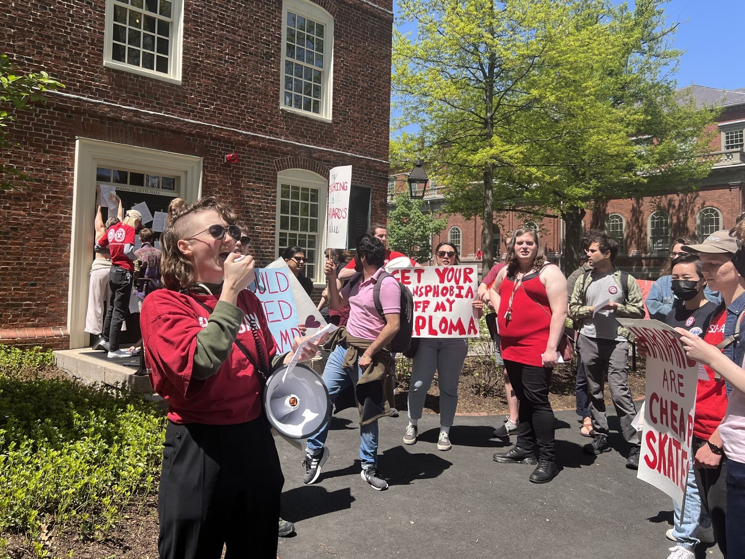Kara Hartig, a student at the Graduate School of Arts and Sciences, leads a chant in front of Massachusetts Hall as rally attendees poster the door.