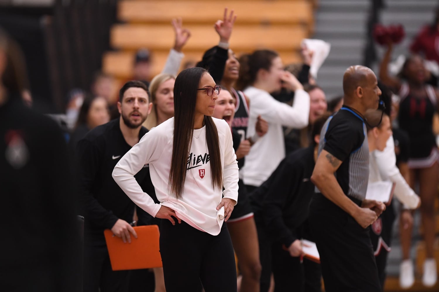 Harvard women's basketball head coach Carrie Moore stands on the sidelines at a 2022-23 season game. The slogan written on her shirt, "Believe It," represents the team's motto during the season.