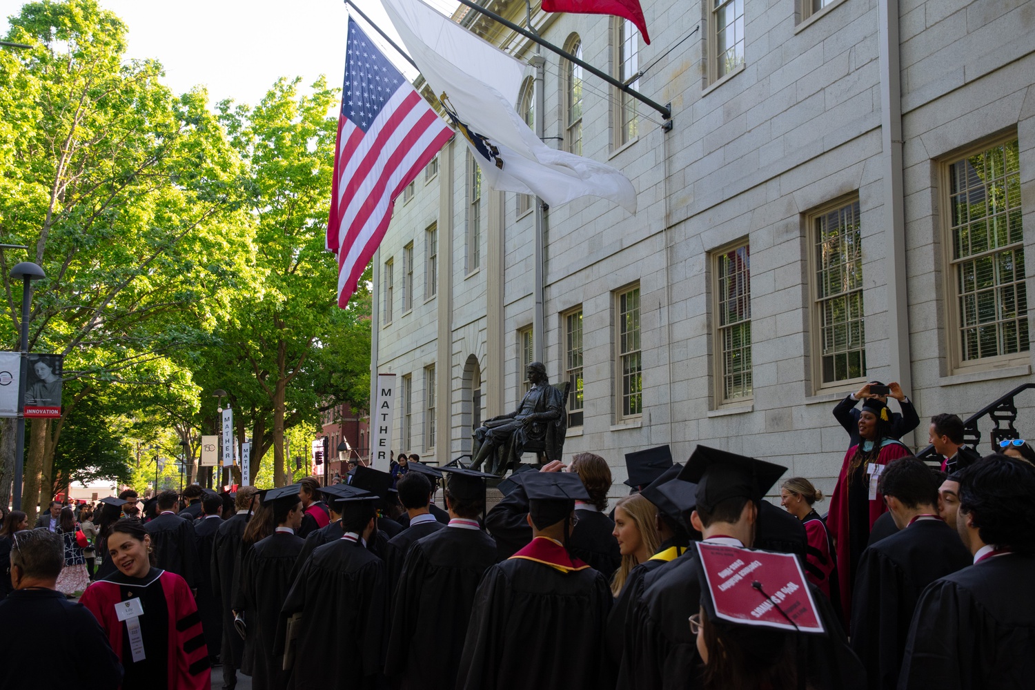 Graduates walk by the John Harvard statute during Commencement 2023.