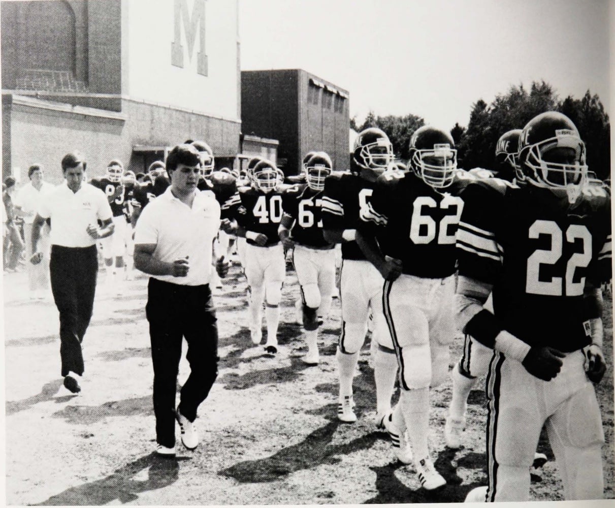 Tim Murphy (back) and then-head coach Buddy Teevens (front) walk alongside the University of Maine football team in 1985. At 28 years old, Teevens was made the youngest head coach in the history of Division I football while at the New England university.