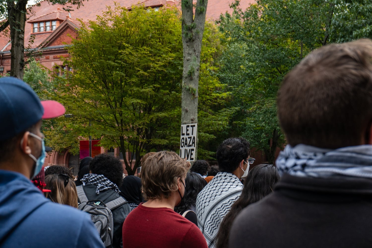 A protester holds a sign stating 'Let Gaza Live' as speakers condemn the Israeli government.