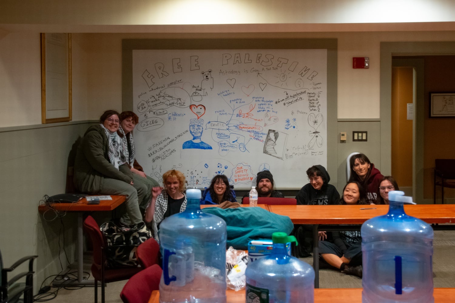 Students occupying University Hall pose for a photo around 1 a.m. in front of a whiteboard they decorated.