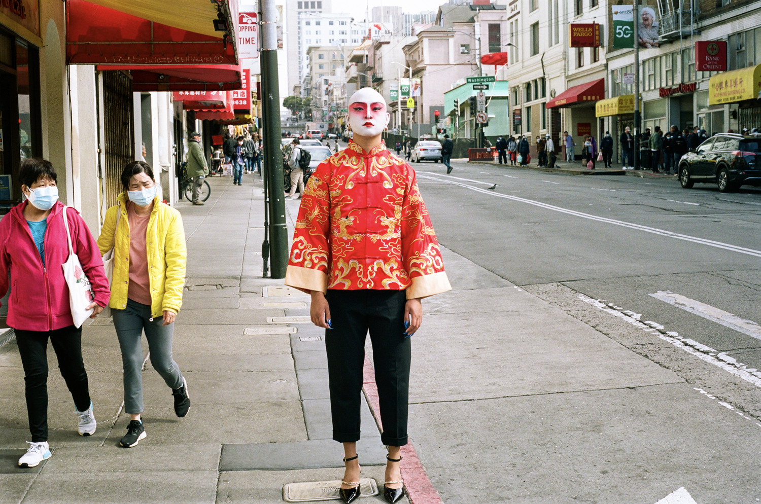 Matta Zheng stands in San Francisco's Chinatown in a qipao and black heels with their face painted white and magenta.