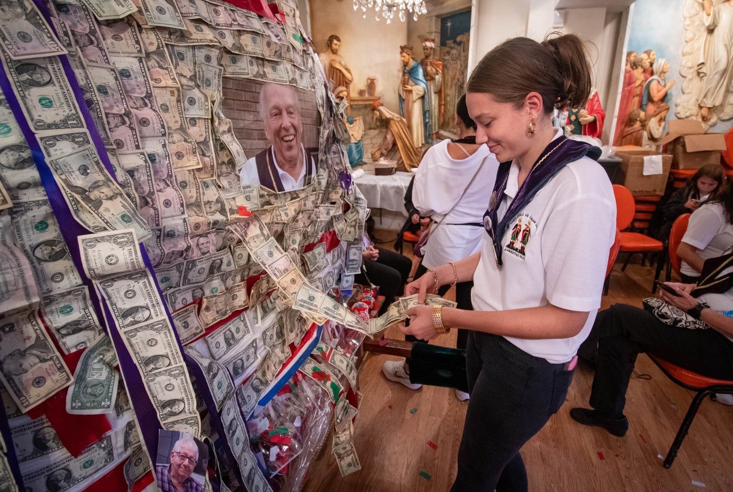 A member of the Saints Cosmas and Damian Society pins money to the statues of the patron saints at the chapel in East Cambridge.