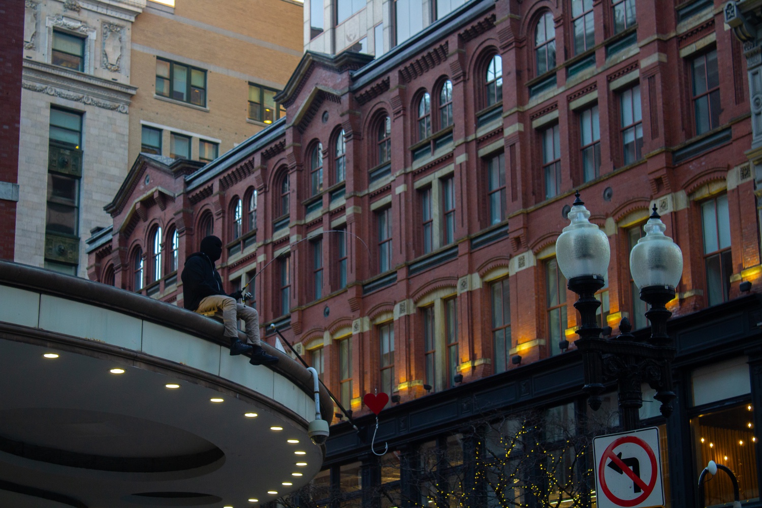 The hyperrealistic statue of a sitting man could easily go unnoticed if it weren’t for the hanging fishing hook with a red heart swaying in the strong winter winds.