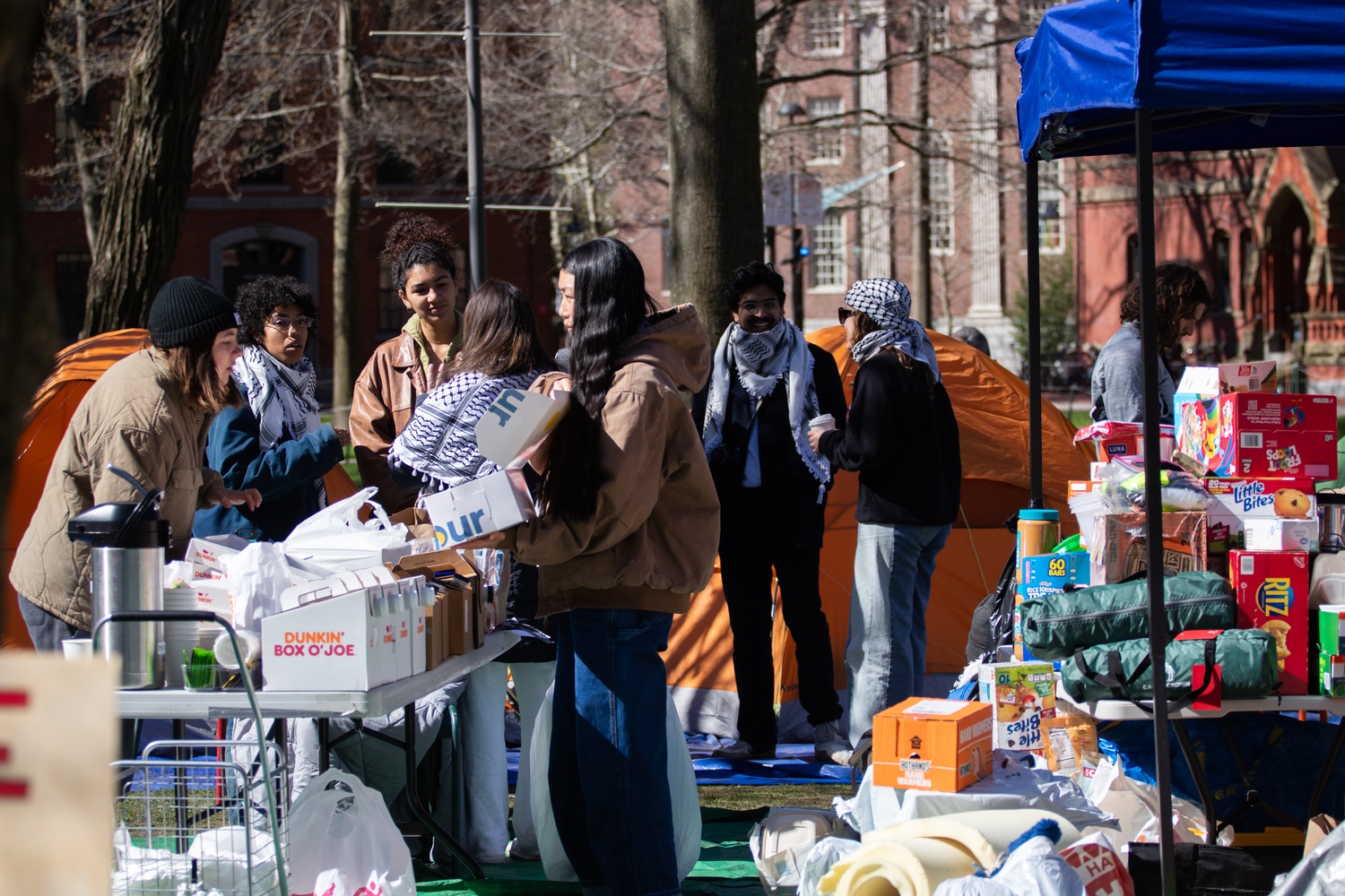Pro-Palestine encampment members show each other breakfast options from Flour Bakery and Cafe over cambros of Dunkin' coffee Thursday morning.