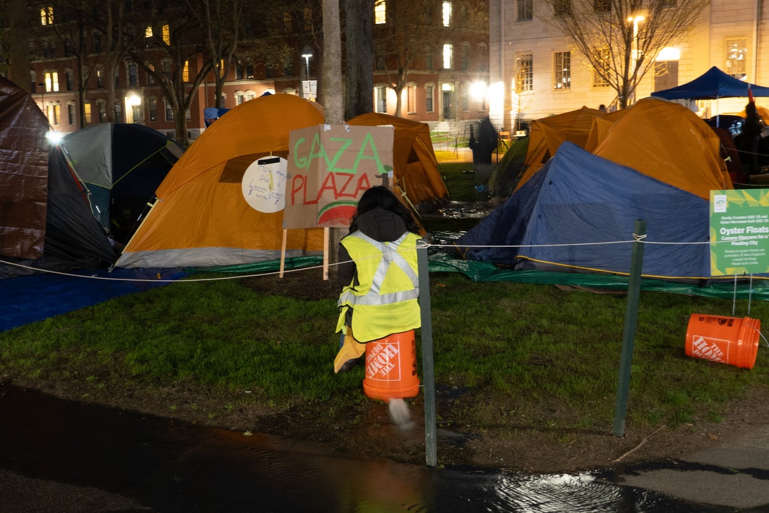 A protestor sits on a bucket covering a sprinkler as water pools on the pavement early Thursday morning.