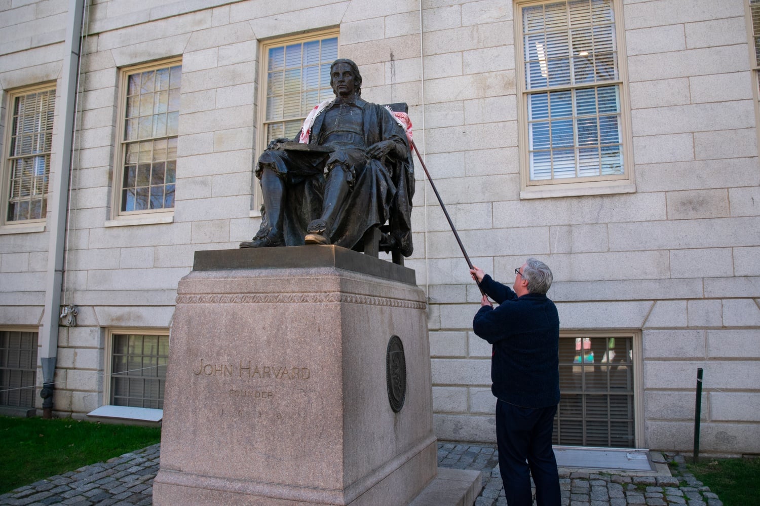 Harvard College Dean of Students Thomas Dunne uses a pole to remove the keffiyeh protesters had placed on the John Harvard statue.