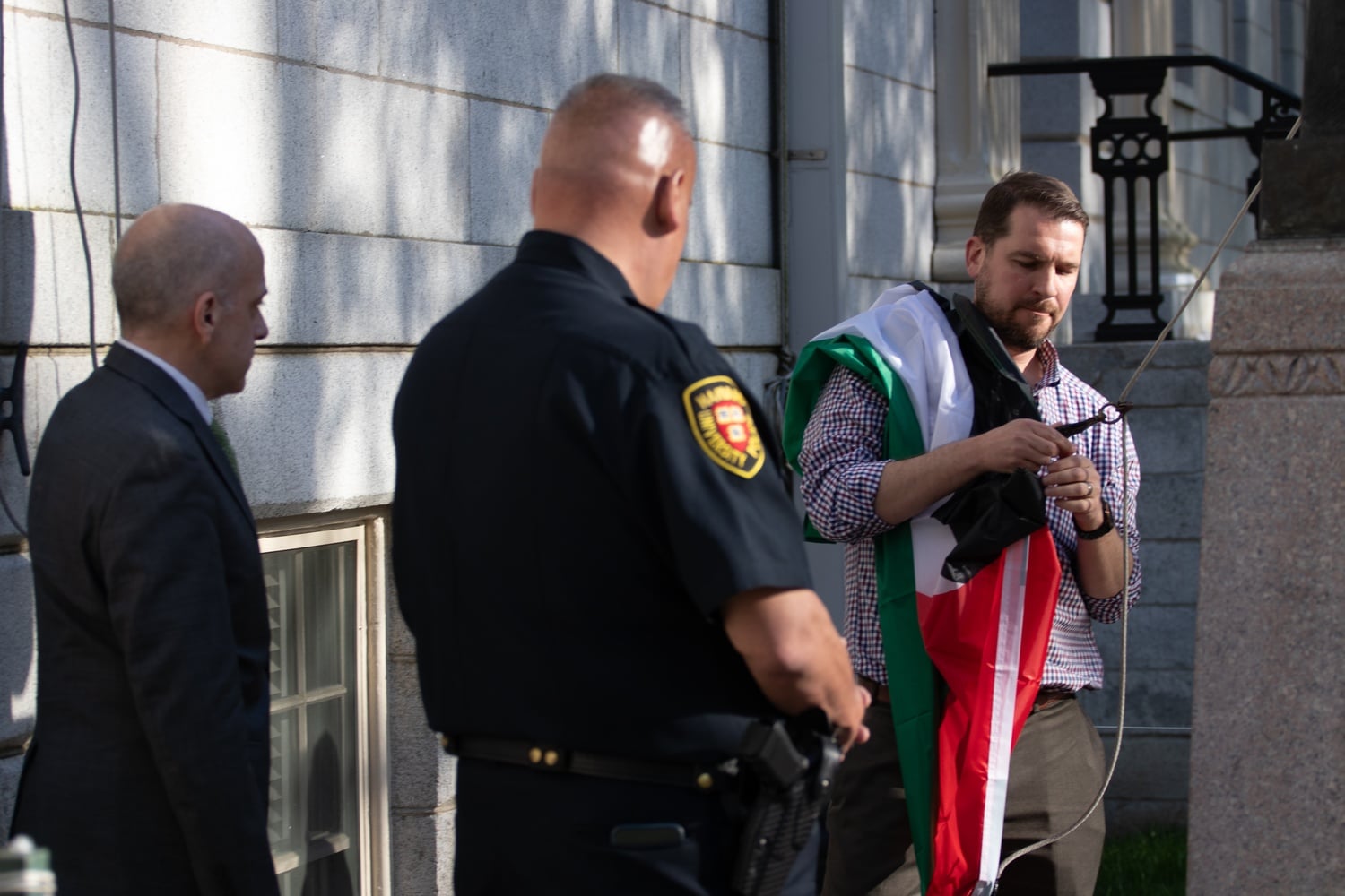 An administrator unhooks the Palestinian flag from the University Hall flagpole as Dean of Student Services Michael Burke and a Harvard University Police officer stand by.
