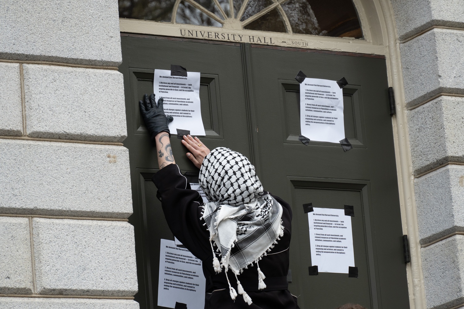 A Harvard Out of Occupied Palestine organizer hangs posters advertising the group's demands, including divestment from Israel, on the door of University Hall.