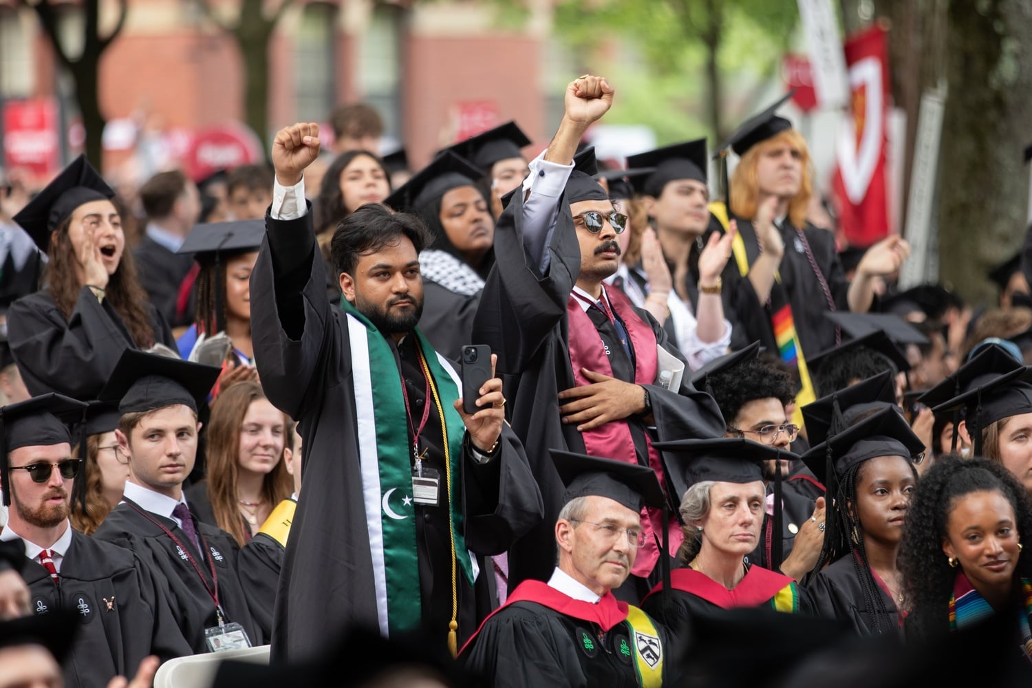 Asmer A. Safi '23-'24 (left), one of the students and pro-Palestine protesters initially denied their degree, stands and raises his fist during Commencement exercises.