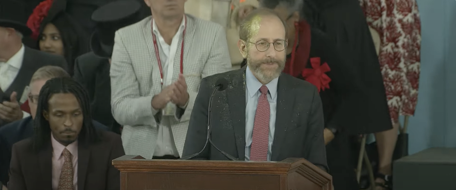 Interim Harvard President Alan M. Garber ’76 stands in front of the podium at Harvard Alumni Day moments after an animal rights protester dumped gold glitter on his face.