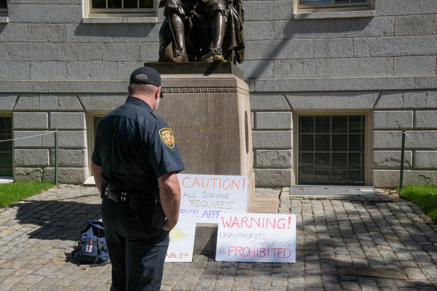 A Harvard University Police Department officer looks at signs and chalk messages written by five Harvard professors in Harvard Yard on Sept. 1. The Faculty of Arts and Sciences will once again permit chalking in campus space.
