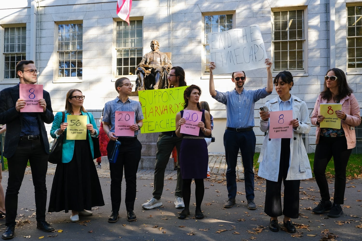 Protesters gathered before the John Harvard Statue Wednesday, holding signs reading "End the Time Caps."