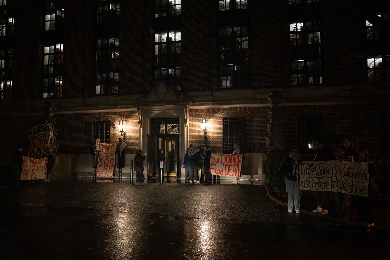 Protesters hold signs reading '40,000 Gazans now are dead' and 'Your donor $s fund death', among others, outside the back entrance to Widener Library.