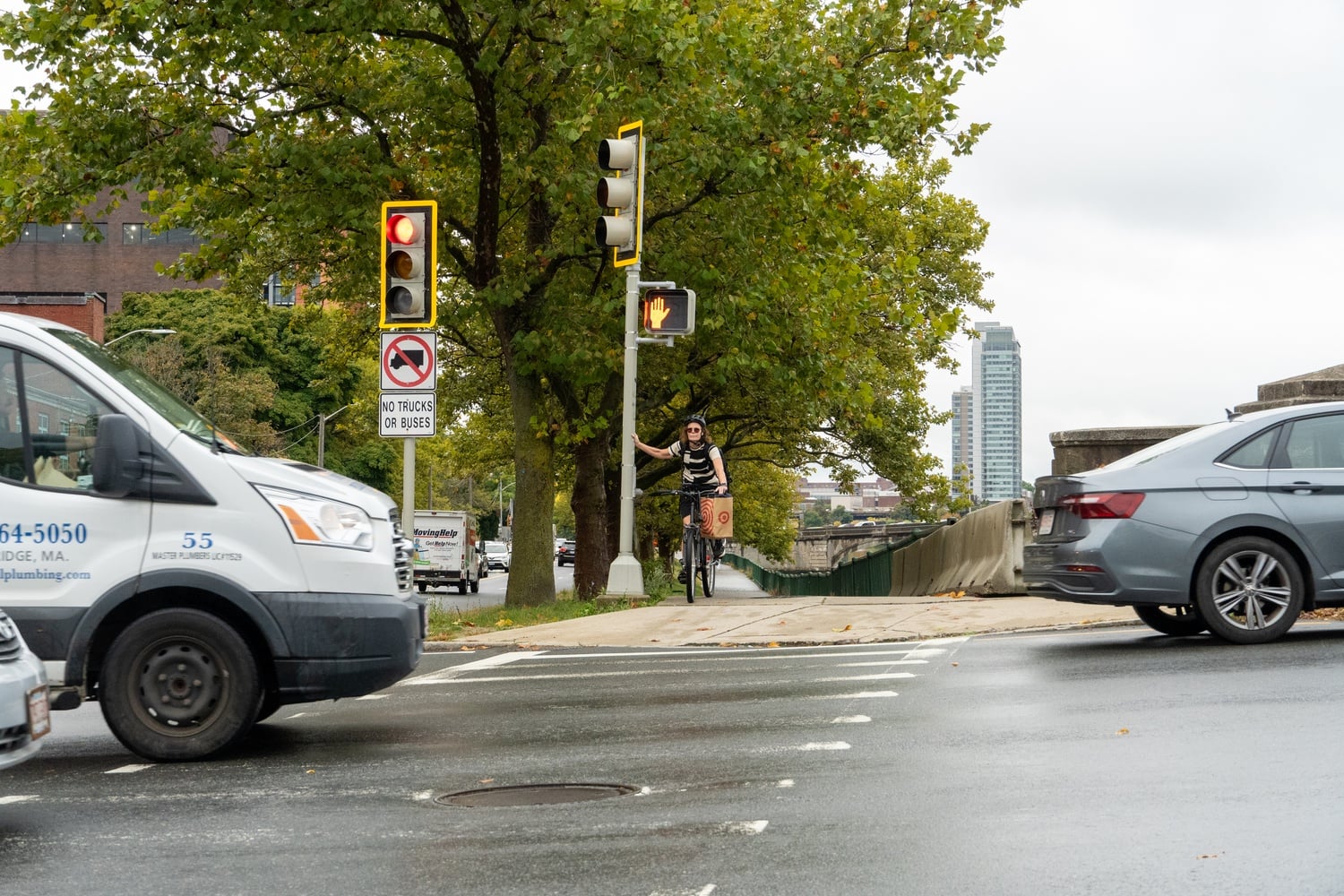 A cyclist stops at a light on Memorial Drive as cars pass over the Western Avenue Bridge.