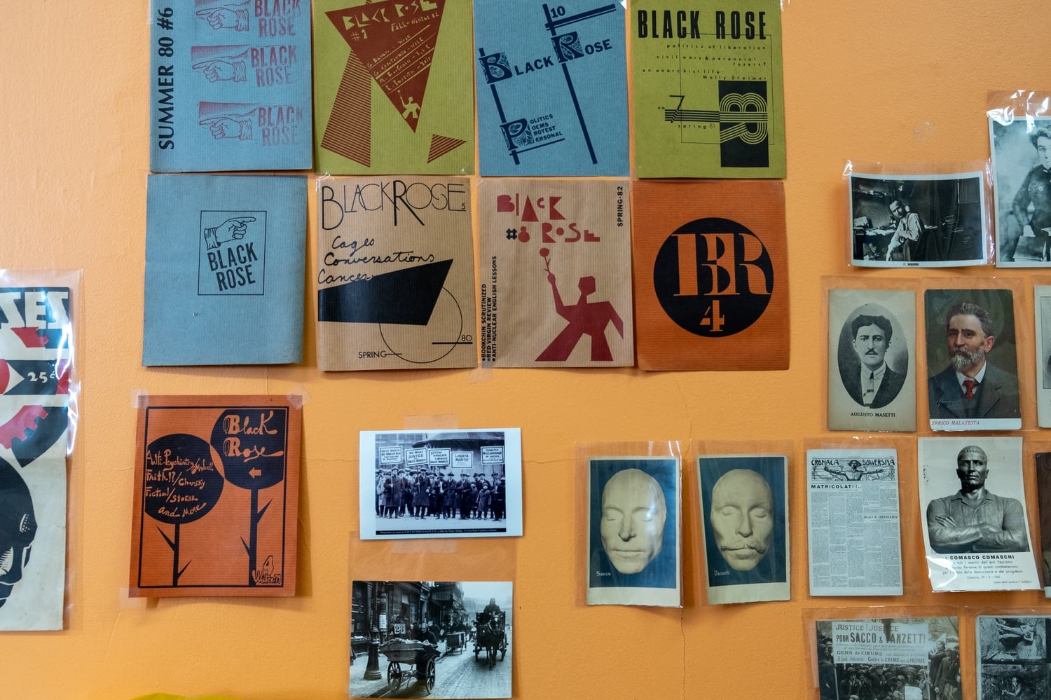 A wall on the third floor, decorated with Black Rose posters and photos of crowds protesting the arrest of Sacco and Vanzetti.