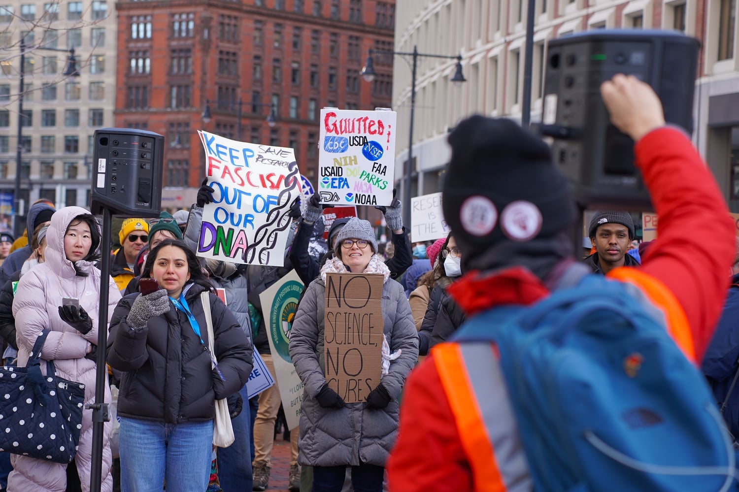 A protester raises their fist at a Wednesday rally against Trump's attempts to freeze federal funding at a John F. Kennedy Federal Building in downtown Boston.