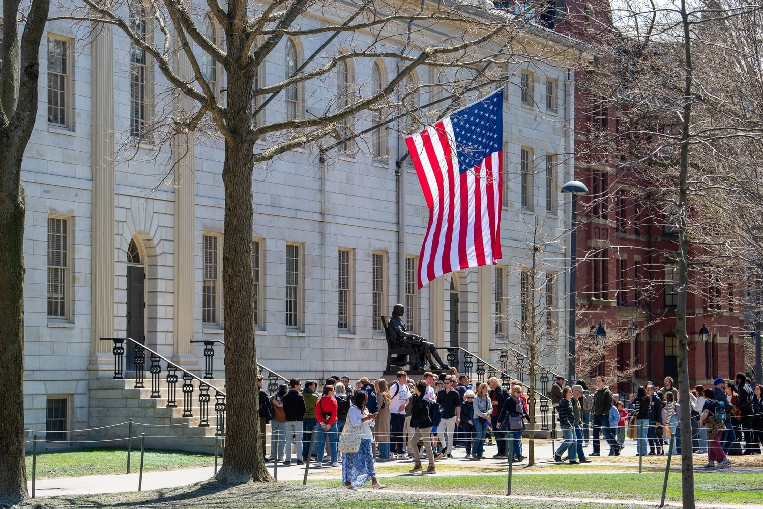 The American flag flies from University Hall over the John Harvard statue and a crowd of students and tourists in April.