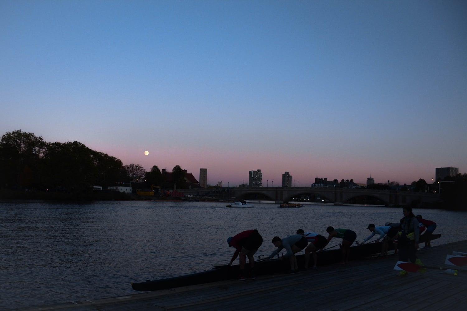 Rowers lift the boat out of the water as the sun sets over the Charles River.
