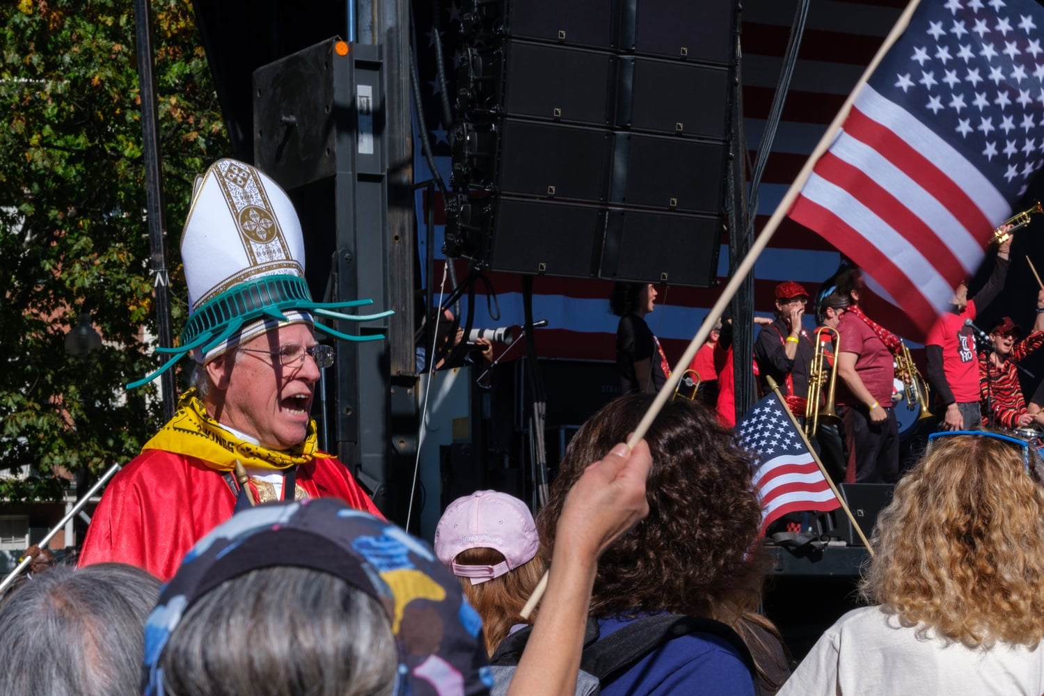 A protester wearing a mitre and a hat resembling the spokes of the Statue of Liberty shouts in a crowd of protesters during No King's protest in Boston Common.